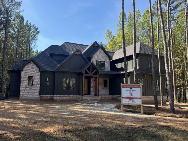 Front of The Lindsey at 3408 Tennyson Court, a Bailey Custom Homes build with dark board-and-batten siding, painted brick, and a timber-framed front porch among tall pines